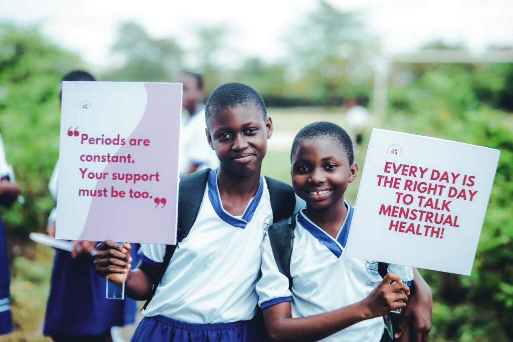 pexels photo 34162722 Two students hold signs promoting menstrual health awareness, smiling outdoors.